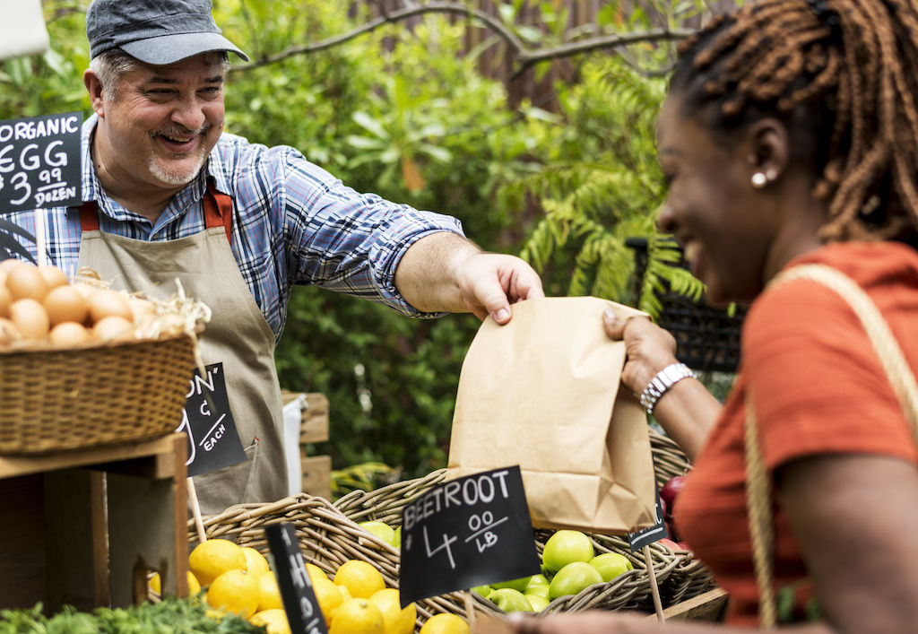 Vendor handing bag of vegetables to customer at farmers market